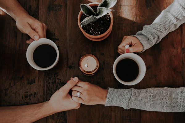 Overhead view of coffee cups and people holding hands.