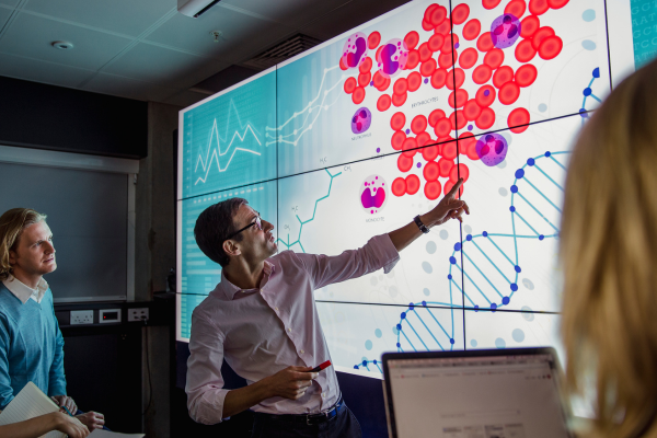 An image of a doctor pointing to a screen highlighting an example of a cancer cell.