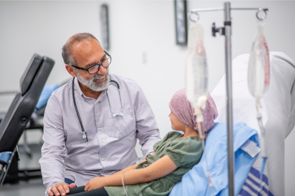 A doctor sits with a young child who is lying a in hospital bed.