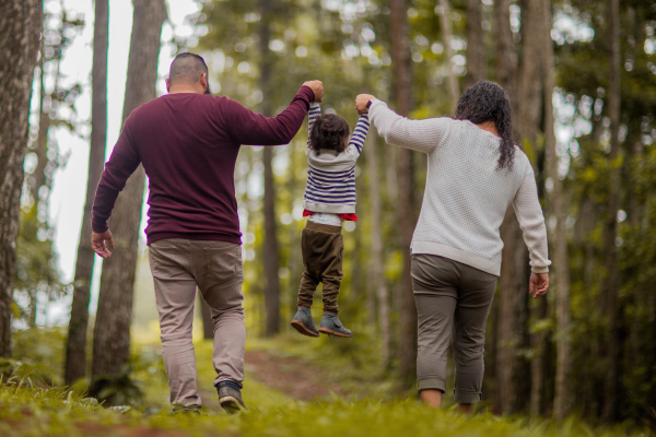 A mother and father walk in the forest with their young child.