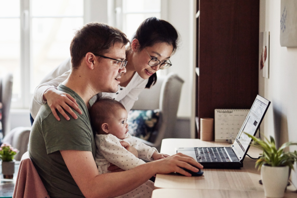 A man, his wide and child sit at a desk reading a computer.