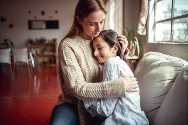 A mother and daught embrace while sitting on a couch.