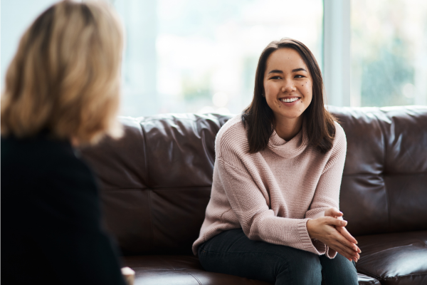 A women sitting on a couch smiling and talking to someone.