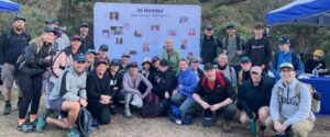 A photo of a group of people smiling in front of the In Honour wall at The Kosi Challenge