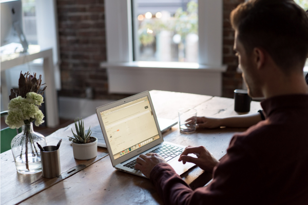 A man sits at his dining room table reading his laptop.